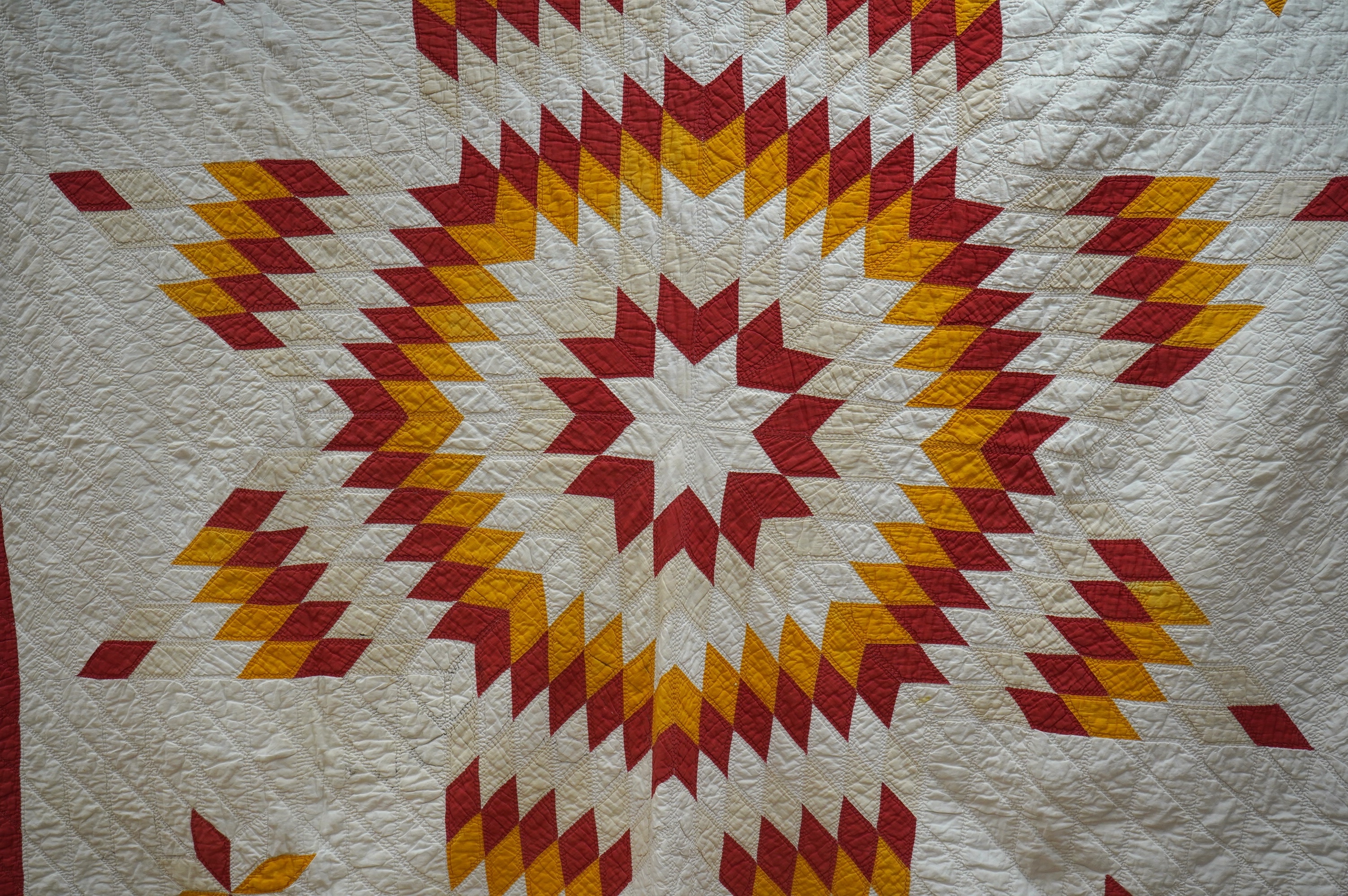 A late 19th century / early 20th century American ‘Star of Bethlehem’ quilt, worked on a plain light cream ground with red and yellow and beige patchworks forming a large double line star with a simple single red inner l